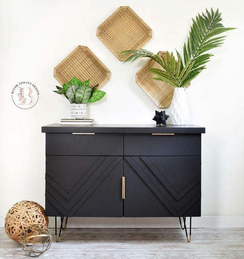 Dixie Belle Paint Caviar Chalk Mineral Paint is the perfect paint for any DIY project!
Entertainment center cabinet painted in Caviar Chalk Mineral Paint with gold hardware. Staged with woven trays mounted on the wall with two potted house plants on a white and gray wood floors.
