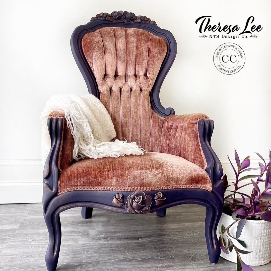 Dixie Belle Paint Chameleon Wax gives your furniture DIY project an iridescent glow and is sheer wax utilized to unveil the  highlight of your project!
Beautiful Vintage cushioned chair with brown wood body and a copper colored cushion. The  Chameleon Wax is seen on the flower applique that is on the base of the chair and the very top. Stage in front of a white wall and a white blanket is on the chair hanging slightly out.