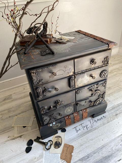 Dixie Belle Paint Chocolate Chalk Mineral Paint is the perfect paint for any DIY project!
Steampunk style of a chest of drawers painted in Chocolate Chalk Mineral Paint with gear aplique on the drawers and the Steampunk Transfer all over piece as well. Staged with antique keys and branches with vintage photo around piece.