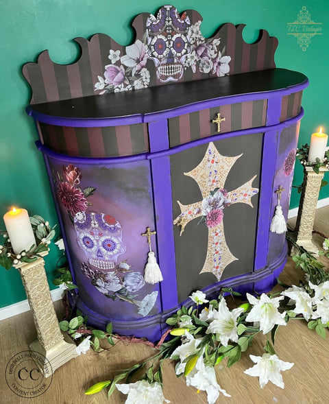 Dixie Belle Paint Company Coffee Bean Chalk Mineral Paint is perfect paint for any DIY project!
There is a DIY chest high, rounded bar.  It is painted with Coffee Bean CMP.  The trim is purple and has Mexican style transfers of skulls and crosses.  There are two candles on either side of the bar and they resting on tall stone candle holders with lily's scattered on the wood floor.