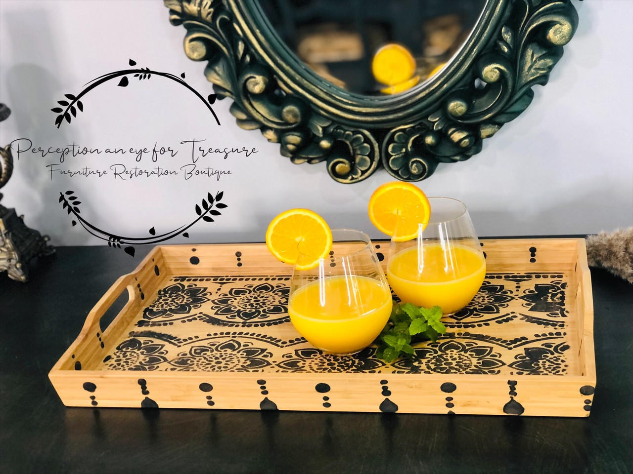 Dixie Belle Paint Coffee Bean Chalk Mineral Paint is the perfect paint for any DIY project!
Resting on top of a dark wood table is a wooden breakfast tray.  The tray has stencils on the bottom done with Coffee Bean CMP.  On the outside and inside of the tray sides are different sized dots.  Inside the tray are two glasses of orange juice with and orange garnish on the rim of the glasses.  There is a gilded, oval mirror behind the tray.