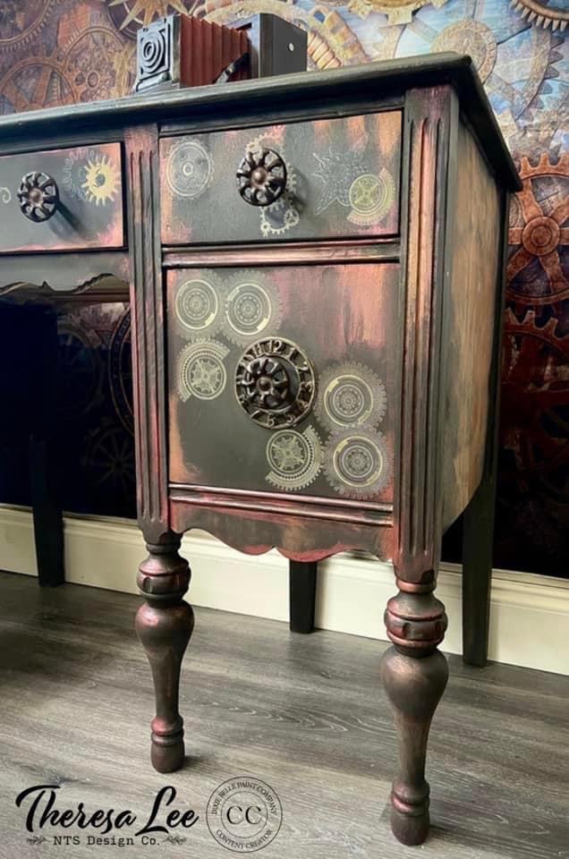 Dixie Belle Paint Coffee Bean Chalk Mineral Paint 
There is a desk that is painted in Coffee Bean CMP and accented with rust paint.  There are gears on the drawers that have come from one of Dixie Belle's transfers.  The drawer handles are round and metal.  There is an old fashioned camera on top of the desk.  The desk sits on a bleached hardwood floor and sits in front of a wall with wallpaper that has metal, gothic gears of all sizes on it.