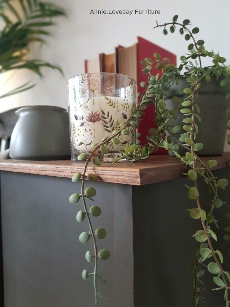 Dixie Belle Paint Collard Greens Chalk Mineral Paint is the perfect paint for any DIY project!
This table is painted with Collard Green CMP.  The top is left to it's wood surface. On top of the table is a clay flower pot painted in the same color as the desk with a long, leafy plant extending down the table.  it also has a white candle and 3 books on the table.