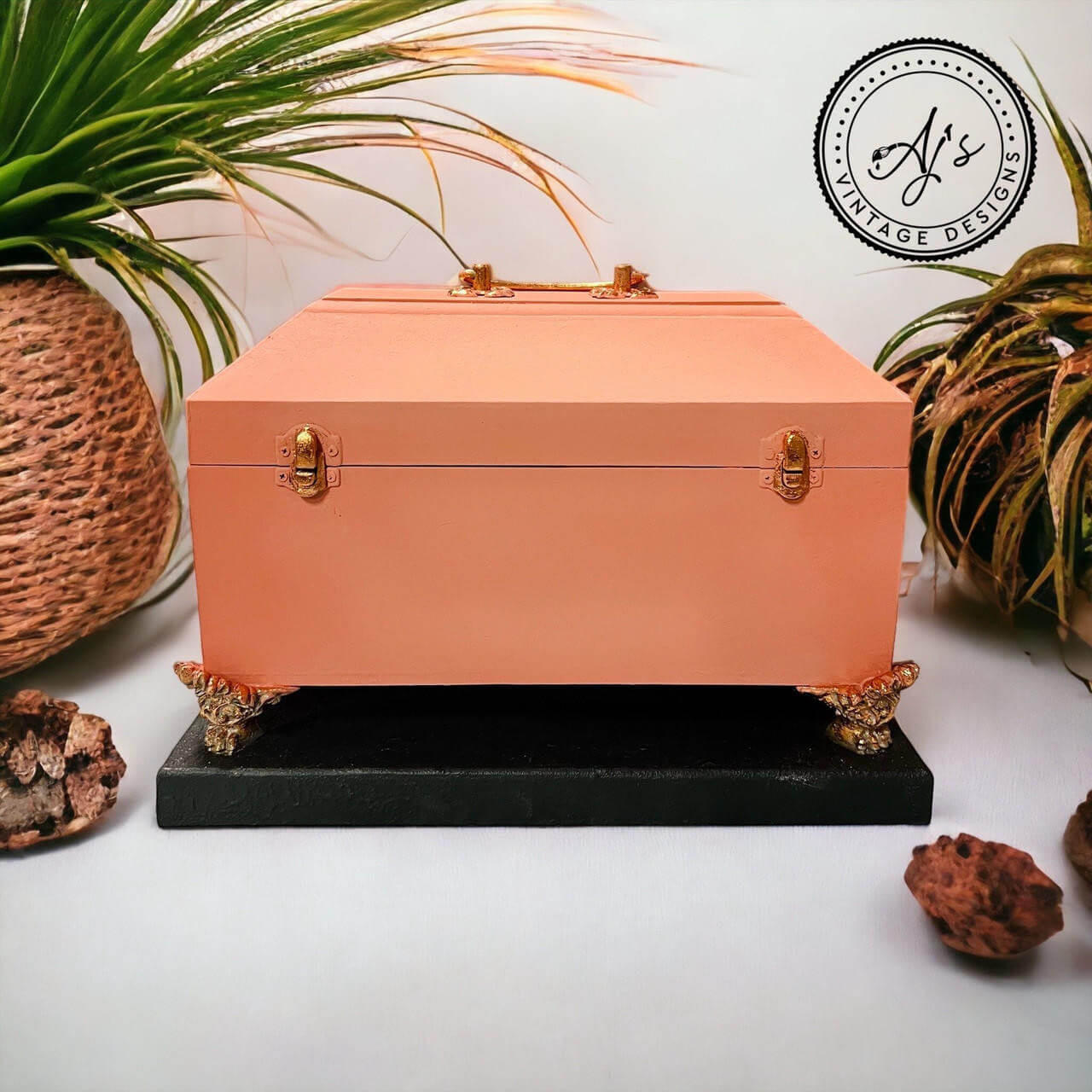 Coral chalk painted jewelry box with gold feet, hinges, and handle. Staged on a black base.