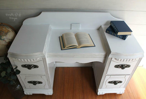 Dixie Belle Paint Cotton Chalk Mineral Paint is the perfect paint for any DIY project!
This is a picture looking down on a gothic desk painted cotton CMP.  There is a book opened up in the center of the desk and two blue books on the back right of the desk.  There is a white lap ship wall behind the desk and a large globe resting on the ground to the left of the desk.  In front of the globe is a glass bottle with leaves on a branch coming out the top of the bottle.