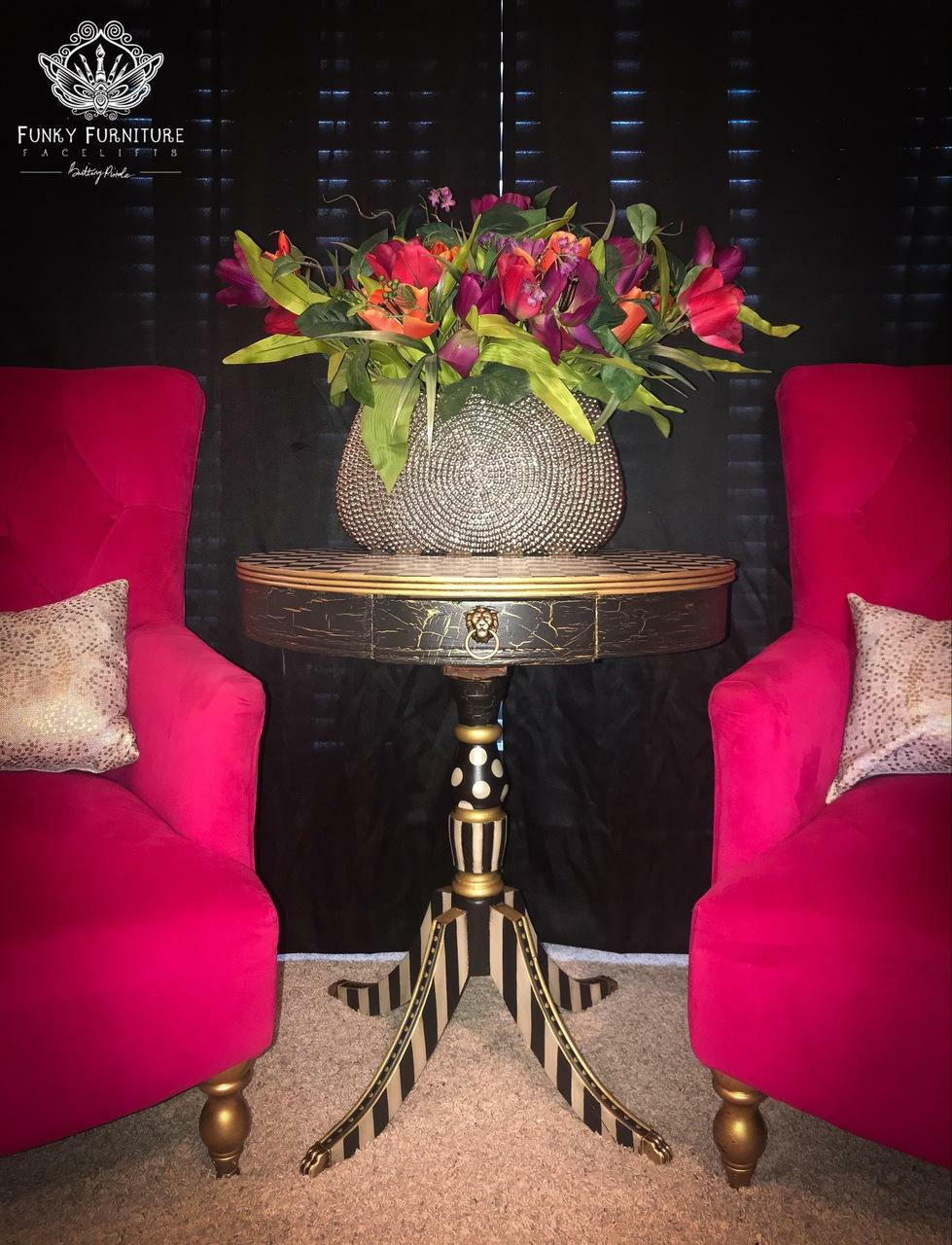 Dixie Belle Paint Crackle. A black painted side table featuring the crackle effect in the paint on the table top. The bottom of the table displays a black and white striped design and the table is staged with 2 pink chairs on both sides.