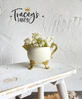 White chalk painted pitcher with gold legs, handle and spout. Staged with white flowers inside, on a white painted distressed stool.