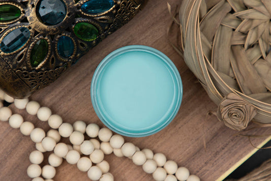 Dixie Belle Paint Dixie Belle Blue Chalk Mineral Paint is the perfect paint for any DIY project!
You are looking straight down on the Dixie Belle Blue CMP container so you are looking directly at the paint since the top is off.  It is staged with white, wooden beads, a jeweled glass, metal box and a wicker basket.  It all rests on a wooden, maple plank.