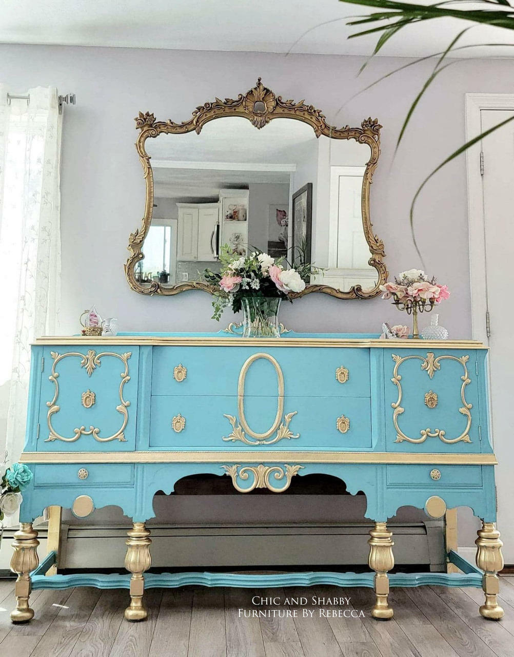 Dixie Belle Paint Dixie Belle Blue Chalk Mineral Paint is the perfect paint for any DIY project!
This is a French, Victorian Style Dresser.  It is painted with Dixie Belle Blue CMP.   There are appliques on both ends and the center of the piece.  The legs are painted in gold just like the appliques and knobs.  There is a gold, ornate mirror on the wall above the dresser and on top it is staged with flowers.