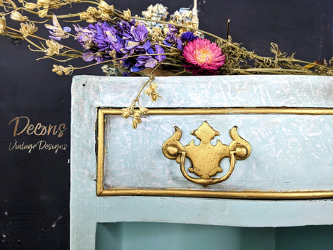 Dixie Belle Paint Dixie Dirt-4oz. 
Corner of dresser Painted blue marble with gold hardware and gold panel around drawer with Dixie Dirt around paneling. Staged on top of dress is a bundle of dried wildflowers.