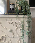Dixie Belle Paint Dixie Dirt-4oz. 
Image shows corner of white dresser piece with Dixie Dirt on woodwork applique on drawers . Staged with two black books with a black candle on top of dresser with a plant pot with faux succulent plant hanging over everything above books.