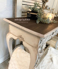 Dixie Belle Paint Dixie Dirt-4oz. 
Image shows console table edge with white base and a brown stained top. The white base of table is distressed using Dixie dirt giving it a rustic/farmhouse style. Staged under the table is wooden basket with a white blanket hanging out.