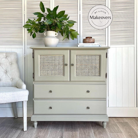 Dixie Belle Paint Dried Sage Chalk Mineral Paint is the perfect paint for any DIY project!
Cabinet with cane webbing doors above drawers painted in Dried Sage Chalk Mineral Paint. Staged on wood floors and a white door panel background. On top has a white vase with handles and greenery.