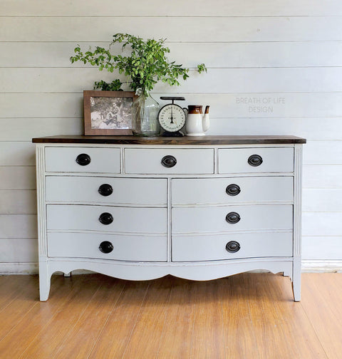 Dixie Belle Paint Driftwood Chalk Mineral Paint is the perfect paint for any DIY project!
Gray chalk painted dresser with stained wood top and black handles. Staged with a photo, clock, vase with greenery and a tea pot.