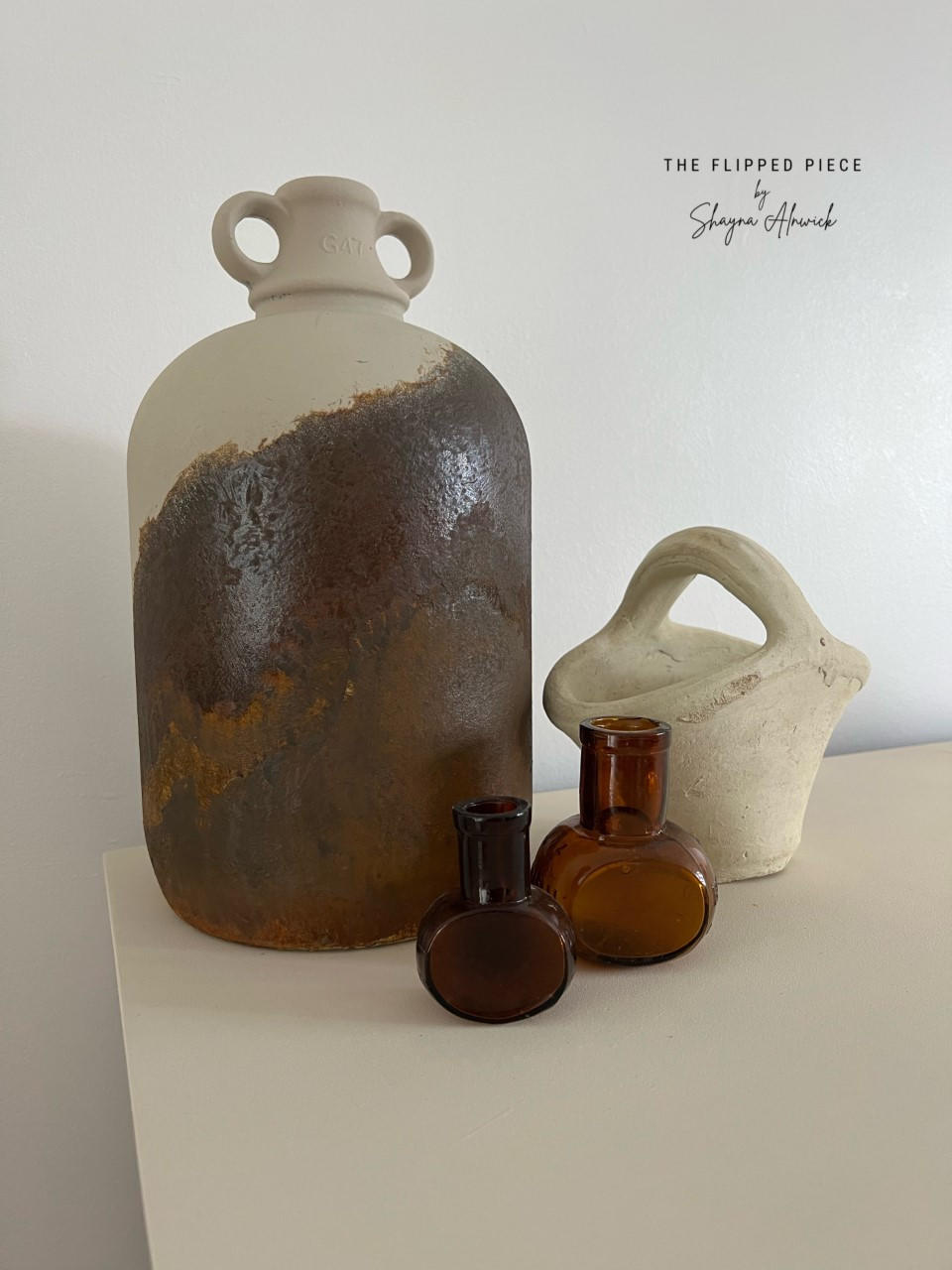 Dixie Belle Paint Drop Cloth Chalk Mineral Paint is the perfect paint for any DIY project! White chalk painted furniture with a large vintage rusted jug, along with a white clay basket and two small glass vases.