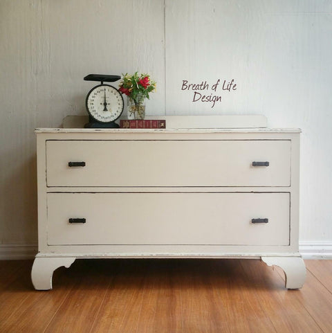 Dixie Belle Paint Drop Cloth Chalk Mineral Paint is the perfect paint for any DIY project! White chalk painted chest with drawers with black handles. Staged with a large vintage food scale and a vase with red roses placed on a book.