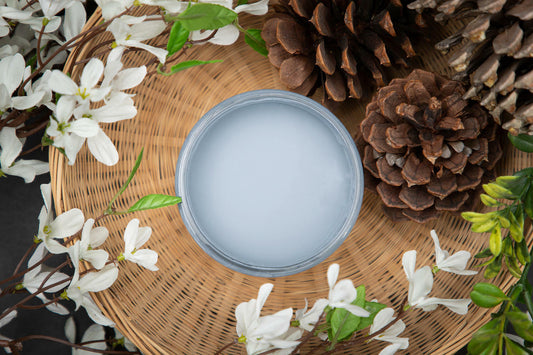 Dixie Belle Paint Dusty Blue Chalk Mineral Paint is the perfect paint for any DIY project! Open jar of Dusty Blue Chalk Mineral Paint staged in a woven basket with white flowers, greenery, and pine cones.