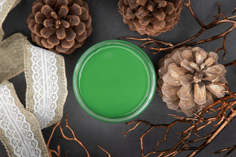 Dixie Belle Paint Evergreen Chalk Mineral Paint is the perfect paint for any DIY project! Open jar of Evergreen Chalk Mineral Paint. 3 pine cones surrounding the open jar with a burlap and lace ribbon laying near the jar.