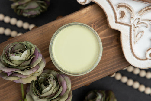Dixie Belle Paint Farmhouse Green Chalk Mineral Paint is the perfect paint for any DIY project!
A look from directly above the paint looking into the paint can.  The paint can is siting on a stained, 2x6 board.  There are two flowers next to the paint can and a white tray on the other side of the paint.  The board is lifted off the ground.  Under the board is a string of wooden balls and two more flowers.
Opened container of Farmhouse Green Chalk Mineral Paint staged with mute green and purple roses on top 