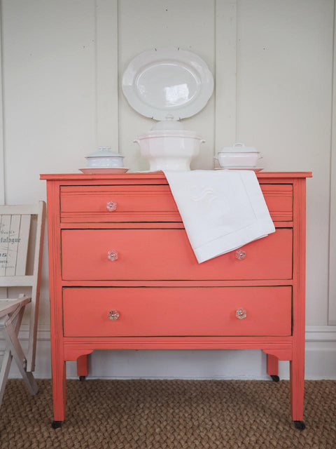 Dixie Belle Paint Flamingo Chalk Mineral Paint is the perfect paint for any DIY project!
Dresser painted in Flamingo Chalk Mineral Paint with crystal hardware, staged with white dishes and pots on top of the piece.