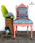 Dixie Belle Paint Flamingo Chalk Mineral Paint is the perfect paint for any DIY project!
A chair painted with  Flamingo Chalk Mineral Paint and blue multicolored cushion with a pattern. Staged against a white wall with a tall woven basket with greenery and flowers.