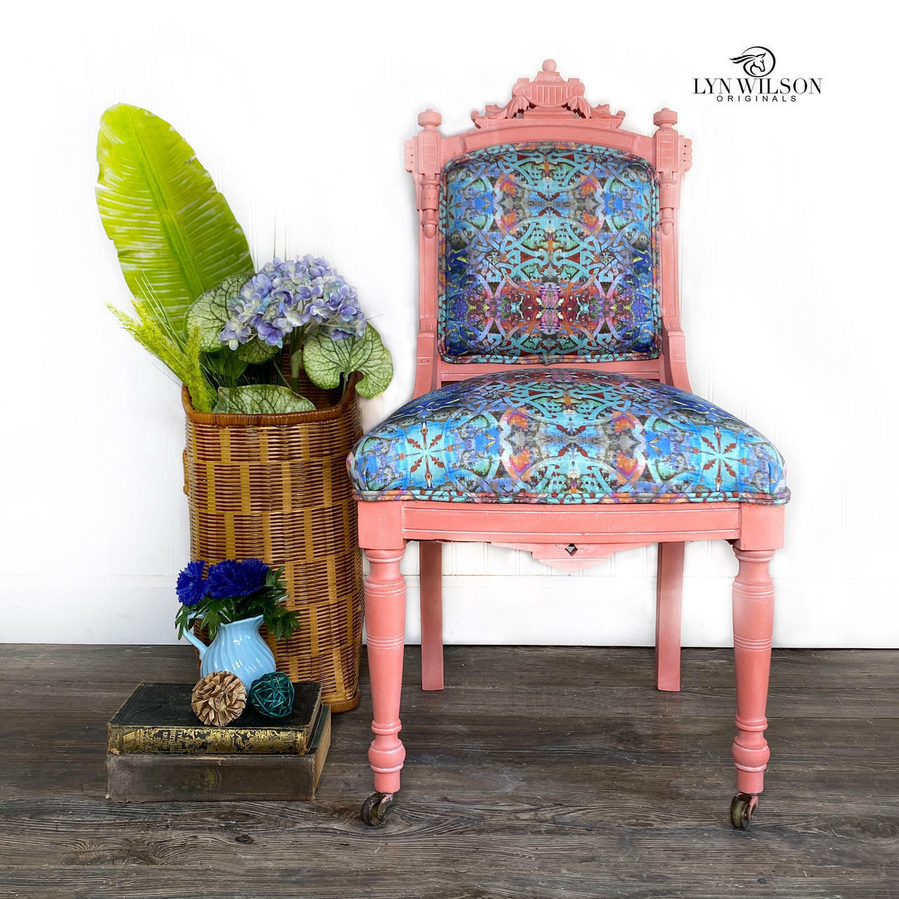 Dixie Belle Paint Flamingo Chalk Mineral Paint is the perfect paint for any DIY project!
A chair painted with  Flamingo Chalk Mineral Paint and blue multicolored cushion with a pattern. Staged against a white wall with a tall woven basket with greenery and flowers.