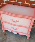 Dixie Belle Paint Flamingo Chalk Mineral Paint is the perfect paint for any DIY project!
A bedside table painted with aa white center on the top and the drawers with Flamingo Chalk Mineral Paint blended and outlined around the piece. Staged with a brick wall behind.