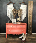 Dixie Belle Paint Flamingo Chalk Mineral Paint is the perfect paint for any DIY project!
Dresser painted in  Flamingo Chalk Mineral Paint with white hardware, staged with angel wings and two curtains meeting at the angel wings hanging on the wall behind the piece. Along with a pair of roller skates in front of the piece with a large ruler plank leaning on the wall.