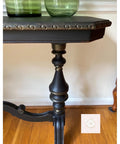 Dixie Belle Paint Gold Shimmer Glaze. Blacks table Leg using Gold Shimmer Glaze in high points and in crevasses to make the the piece have more dimension. Staged  on wooden floor with white wall.