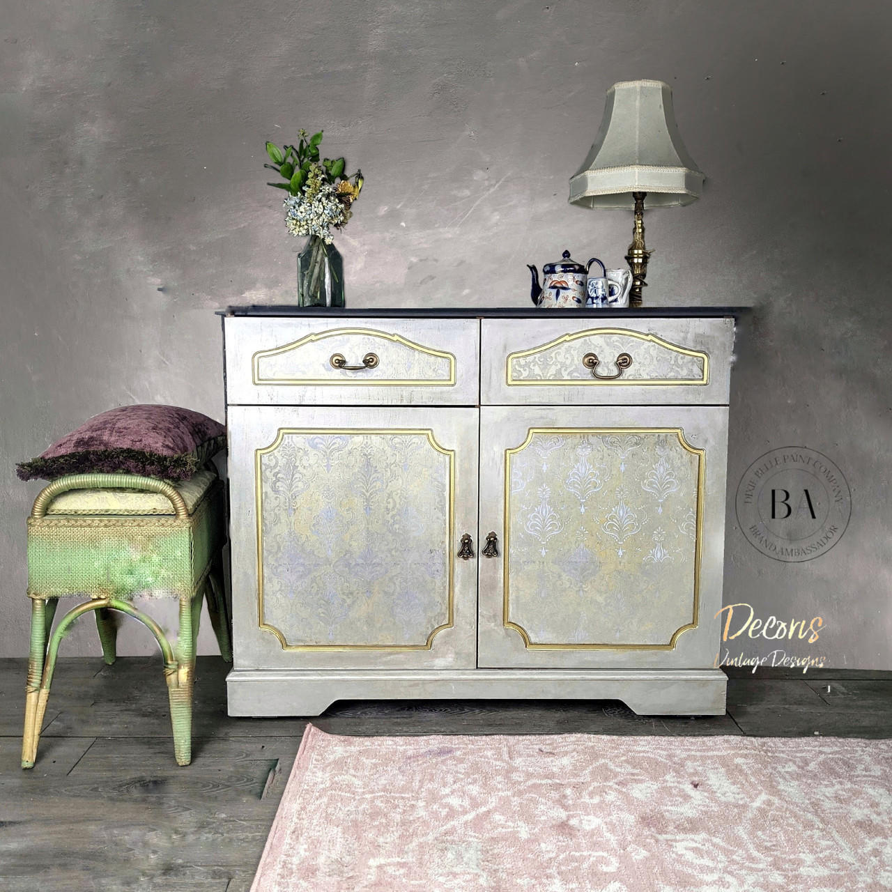 Dixie Belle Paint Gold Shimmer Glaze. White Gray Vanity with Gold Shimmer Glaze used in the indexes of the drawers and doors , to give it an elegant and royal look. Staged with a gold lamp and a porcelain teapot with teacups. Glass see through vase with flowers.