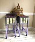 Dixie Belle Paint Gold Shimmer Glaze. Two purple Side tables with Gold shimmer glaze being used to create stripes on top of pieces with gold accents in the nook's of the legs to create more dimension. White and green stripes drawer has floras design around it. Staged on a white washed wood floor with gold temple cage figure on top of tables with a lavender branch hanging in-between tables.