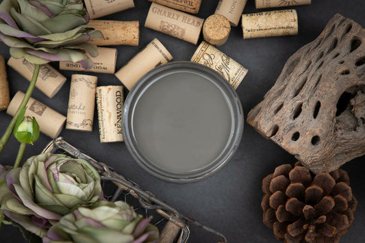 Dixie Belle Paint Gravel Road Chalk Mineral Paint is the perfect paint for any DIY project! Top view of open container of Gravel Road Chalk Mineral Paint. Staged with corks, artichokes, pinecone and driftwood.