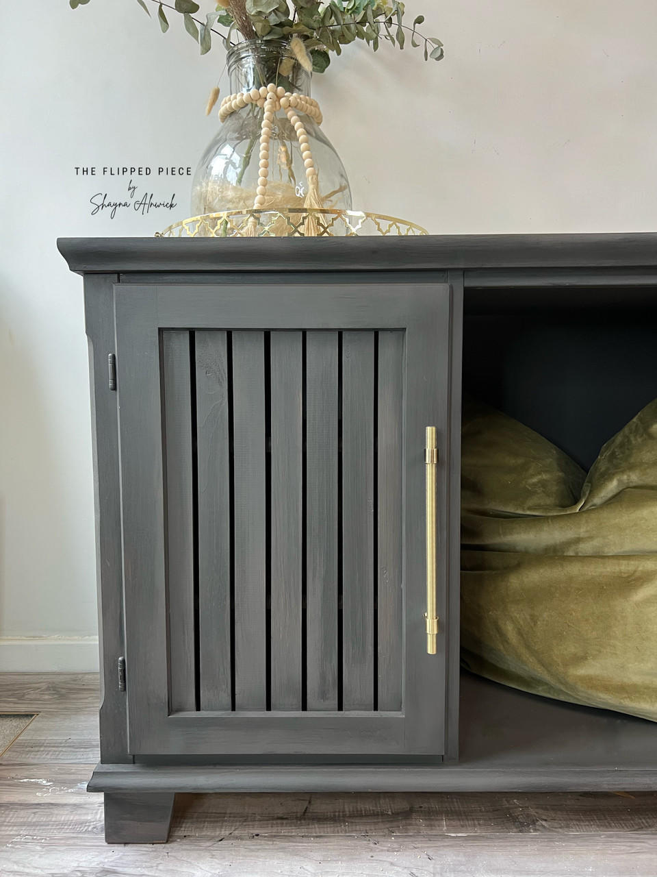 Dixie Belle Paint Gravel Road Chalk Mineral Paint is the perfect paint for any DIY project! Storage Cabinet painted in Gravel Road Chalk Mineral Paint with gold handle. Staged with one door open inside cabinet has green velvet pillow on top of piece is gold plate and glass flower vase.