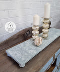 Dixie Belle Paint Haint Blue Chalk Mineral Paint is the perfect paint for any DIY project!
A wooden tray with legs painted with Blue Chalk Mineral Paint  and the Victorian Damask - Stencil in white is seen on the top side of the tray. Staged with two gold candle pedestals with white candles along with a seashell.