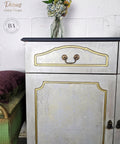 Dixie Belle Paint Hi Ho Silver Glaze 
White vanity using the Grunge Glaze around the piece to give a antique look with gold inside the wood indents. Staged with a glass vase and flowers.