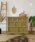 Dixie Belle Paint Holy Guacamole Chalk Mineral Paint is the perfect paint for any DIY project!
Dresser painted with Holy Guacamole Chalk Mineral Paint with bronze hardware staged with feathers, greenery around the piece, a staged latter with lights hanging off the ladder. On top of the furniture are books, vase and miniature 3 pumpkin. A fur gray rug is seen in front of the piece.