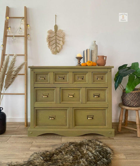 Dixie Belle Paint Holy Guacamole Chalk Mineral Paint is the perfect paint for any DIY project!
Dresser painted with Holy Guacamole Chalk Mineral Paint with bronze hardware staged with feathers, greenery around the piece, a staged latter with lights hanging off the ladder. On top of the furniture are books, vase and miniature 3 pumpkin. A fur gray rug is seen in front of the piece.