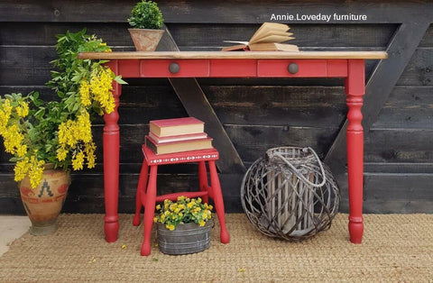 Dixie Belle Paint Honky Tonk Red Chalk Mineral Paint is the perfect paint for any DIY project!
A table with a light wood top and bench both painted in Honky Tonk Red Chalk Mineral Paint staged with yellow flowers and greenery as well as books are seen around and on both pieces of furniture. Staged on a brown rug and a rustic wood background.