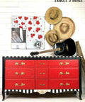 Dixie Belle Paint Honky Tonk Red Chalk Mineral Paint is the perfect paint for any DIY project!
Dresser painted with the drawers painted in Honky Tonk Red Chalk Mineral Paint and the body painted in black with the trims as white & black stripes. Staged with a black acoustic guitar and three straw hats on the wall hanging above the piece to the left has a painting with red hearts.
