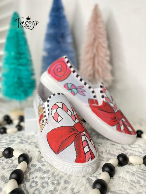 Dixie Belle Paint Honky Tonk Red Chalk Mineral Paint is the perfect paint for any DIY project!
Image shows a pair of slip on sneakers that have candy canes and bows all using the Honky Tonk Red Chalk Mineral Paint. Staged with black and white beads around the sneakers with three miniature Christmas trees in the background.