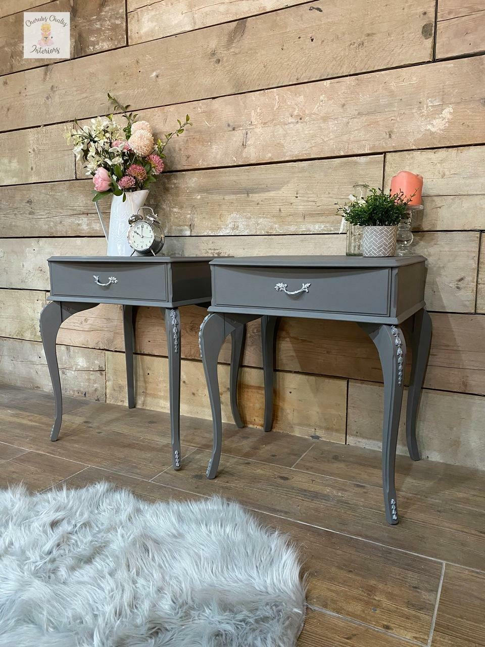 Dixie Belle Paint Hurricane Gray Chalk Mineral Paint is the perfect paint for any DIY project!
Two end tables painted in  Hurricane Gray Chalk Mineral Paint with silver hardware and flowers inside vases with an alarm clock to the right of it is seen on top of the pieces.