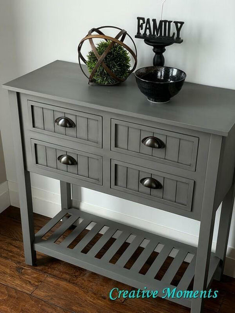 Dixie Belle Paint Hurricane Gray Chalk Mineral Paint is the perfect paint for any DIY project!
An entryway table painted in  Hurricane Gray Chalk Mineral Paint with black hardware. Staged on wooden floors and a white wall, on top of the piece is a black ceramic bowl, a black pedestal with the sign that reads "FAMILY".