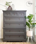 Dixie Belle Paint Hurricane Gray Chalk Mineral Paint is the perfect paint for any DIY project!
Chest of drawers painted in Hurricane Gray Chalk Mineral Paint with bronze hardware,staged with 3 different vases on the top of the piece as well as a standing potted houseplant to the right.