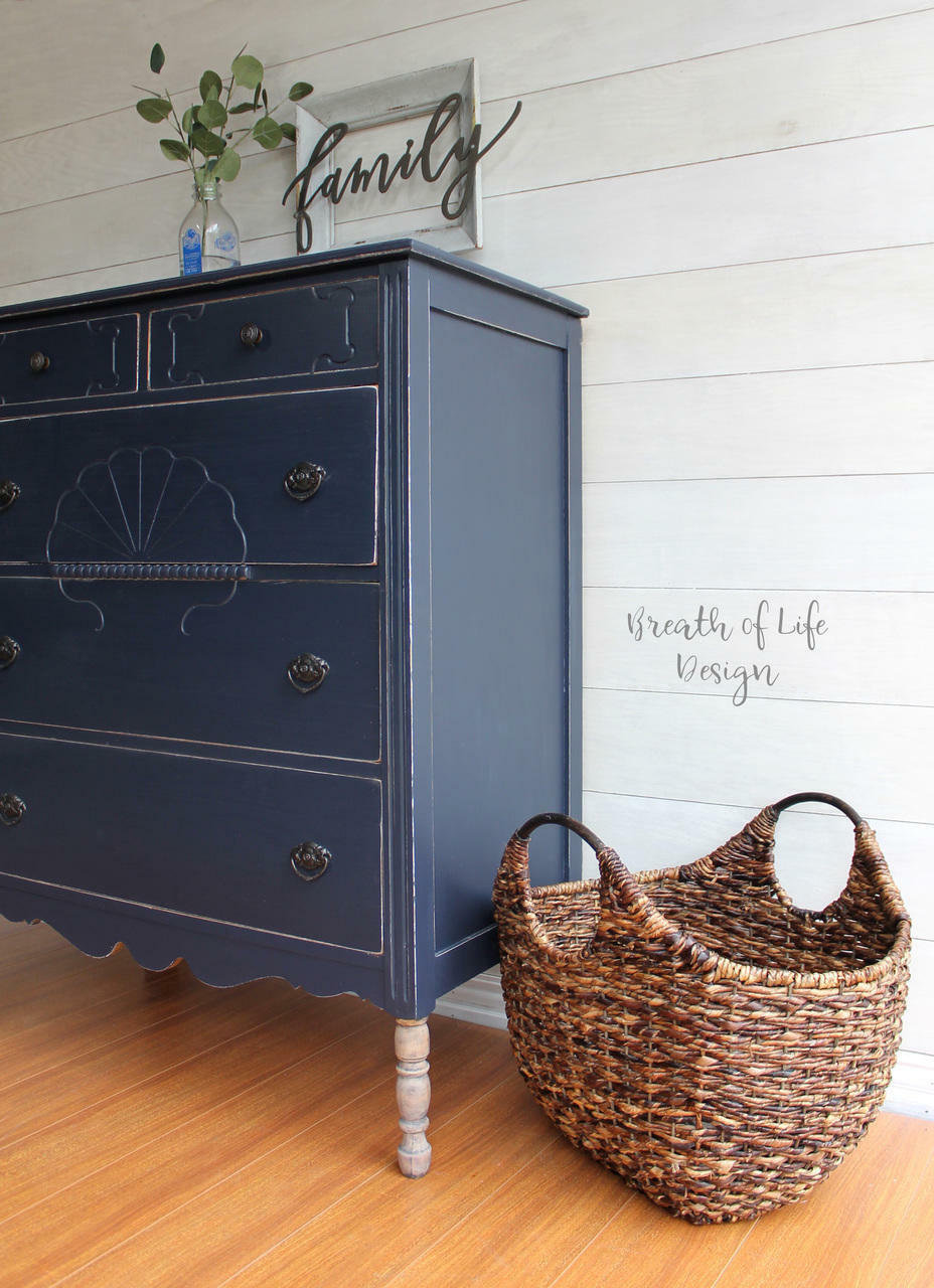 Dixie Belle Paint In the Navy Chalk Mineral Paint is the perfect paint for any DIY project!
A Dresser painted in In the Navy Chalk Mineral Paint  with distressed edges around the dresser. Staged with a woven basket besides the piece along a white wall.