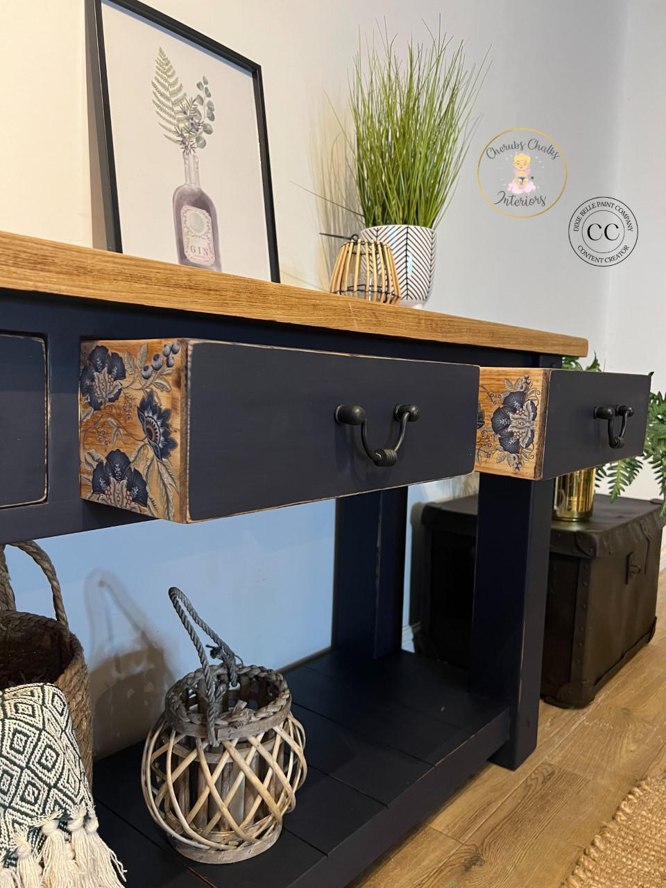 Dixie Belle Paint In the Navy Chalk Mineral Paint is the perfect paint for any DIY project!
A console table painted in In the Navy Chalk Mineral Paint with black hardware and a natural wood top, two drawers are open showing Embroidered Lotus - Transfer on the side panel of the drawer. Staged with decor like potted plants, wooden and woven baskets and a picture frame on top of the piece.
