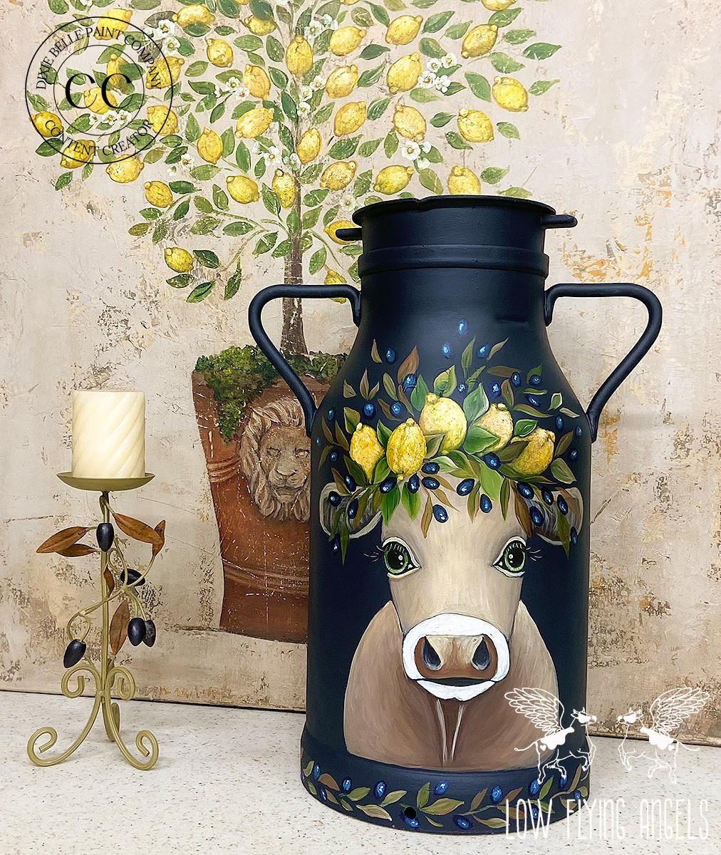 Dixie Belle Paint In the Navy Chalk Mineral Paint is the perfect paint for any DIY project!
Milk church painted in In the Navy Chalk Mineral Paint with a hand painted cow with a lemon, olive and greenery headband. Staged with a lemon tree decoupaged on the wall and a candle holder with olives and leaves around it staged next to the piece.