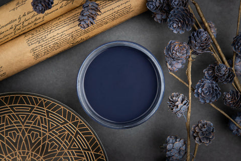 Dixie Belle Paint In the Navy Chalk Mineral Paint is the perfect paint for any DIY project!
A top view of an opened container of In the Navy Chalk Mineral Paint, staged with pinecones painted with In the Navy CMP along with scrolls and a black and old plate.