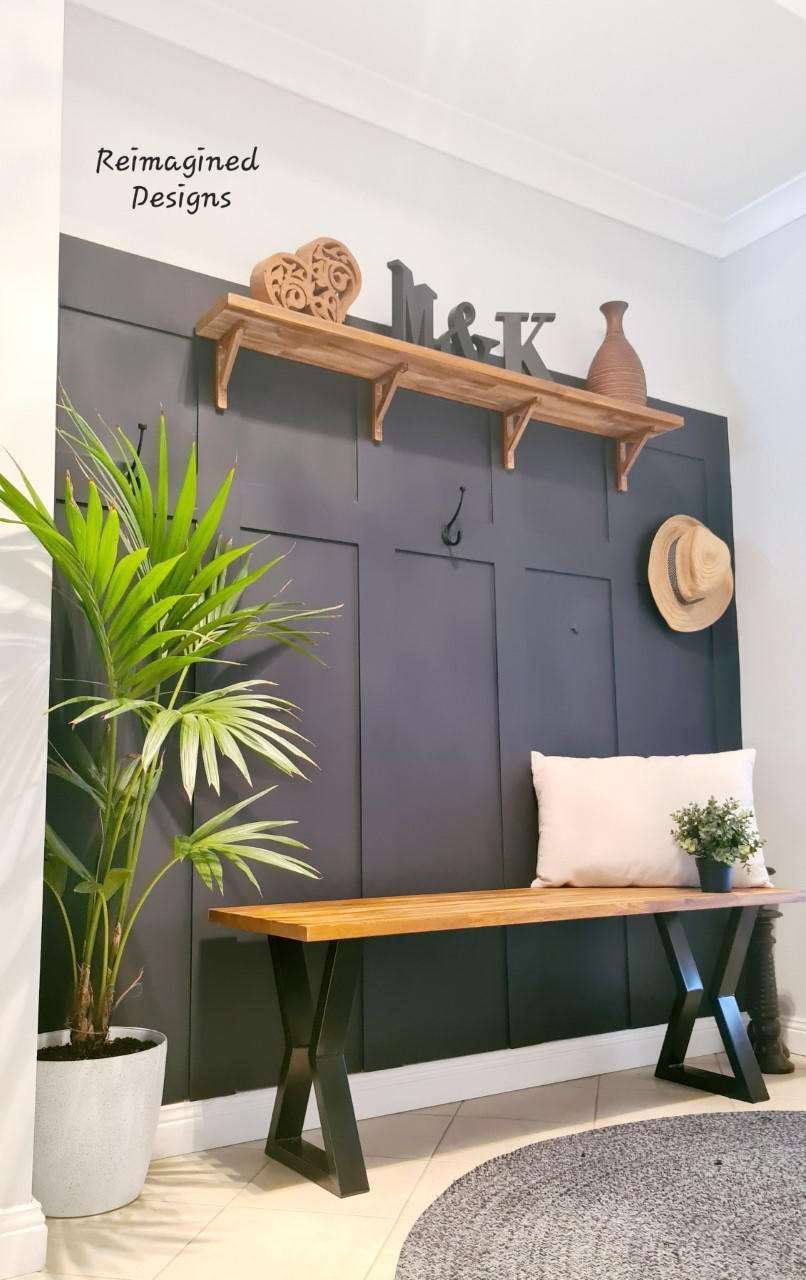 Dixie Belle Paint In the Navy Chalk Mineral Paint is the perfect paint for any DIY project!
A painted wall in a mudroom using  In the Navy Chalk Mineral Paint staged with a wooden shelf and a wooden bench with black legs, a white pillow and potted plant on the bench.