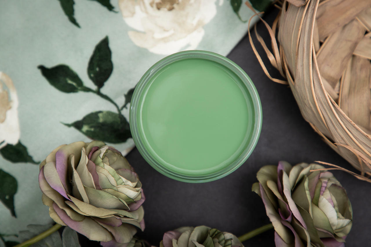 Dixie Belle Paint Kudzu Chalk Mineral Paint is the perfect paint for any DIY project!
Top view of an opened container of Kudzu Chalk Mineral Paint staged with red & purple roses, wooden basket and on top of a white rose pattern cloth.