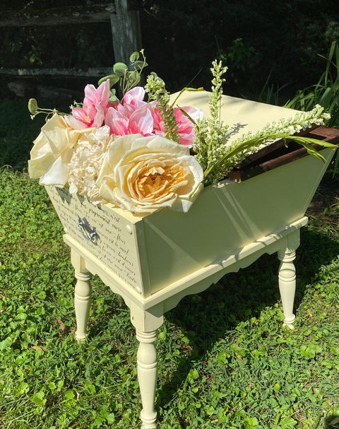 Dixie Belle Paint Lemonade Chalk Mineral Paint is the perfect paint for any DIY project!
Antique dough box painted in Lemonade Chalk Mineral Paint with a dark wood top, Staged with one side open and yellow, pink and leaves are seen inside the piece staged outside on grass.